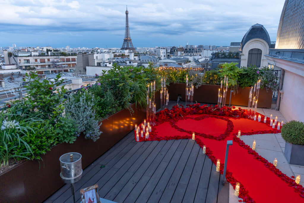 Queen of Hearts romantic proposal setup on the Secret Table rooftop at The Peninsula Paris with red carpet, rose petals, glass candelabras, silk roses, and Eiffel Tower view